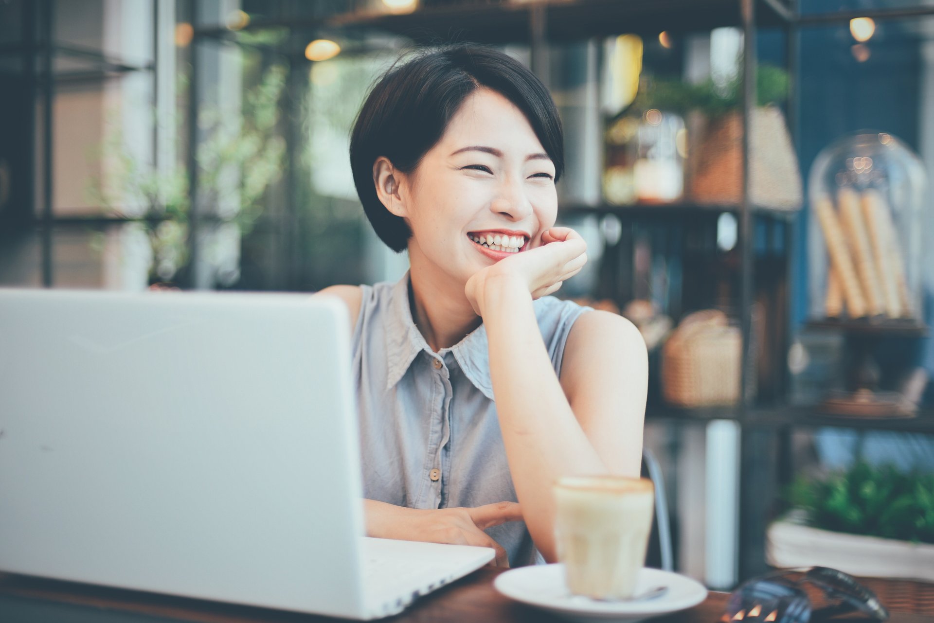 A young Asian woman smiles while working at a laptop computer