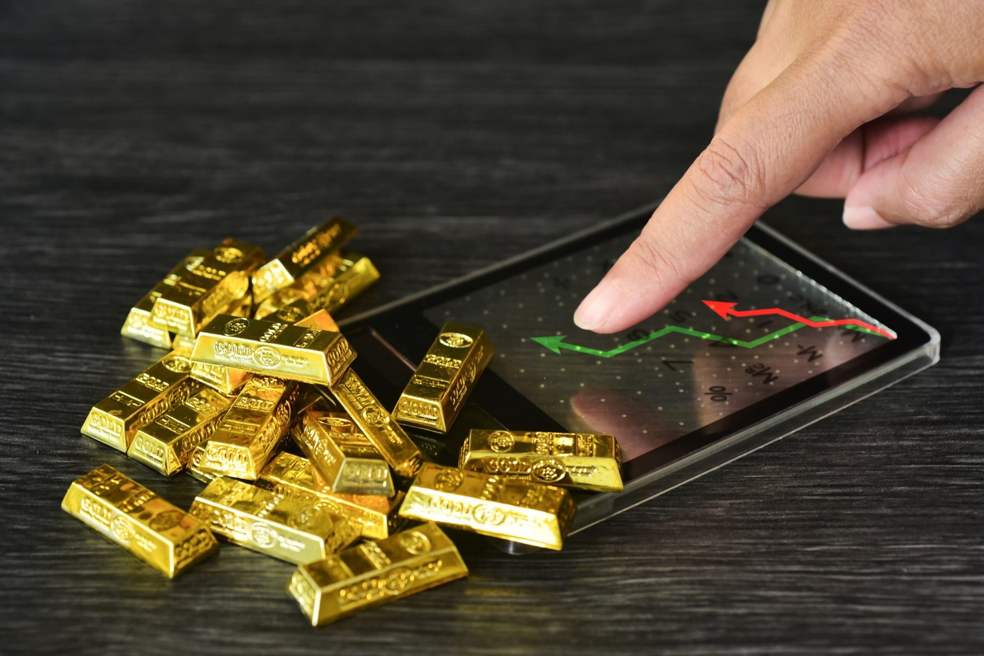 Gold bars next to a calculator with graph showing an increase in gold price.